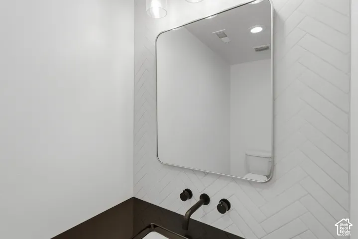 Modern bathroom vanity featuring a sleek rounded-edge mirror with integrated lighting, white subway tile backsplash, matte black wall-mounted faucet fixtures, and a dark countertop with clean-lined design