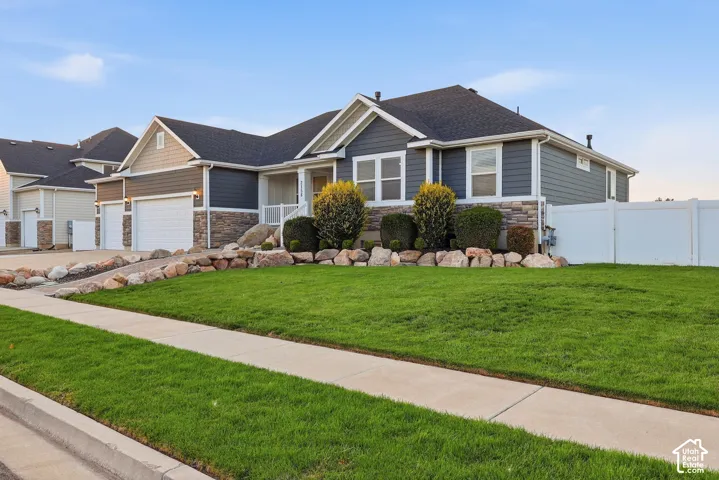 Exterior featuring a stone and siding facade, covered front entry, attached two-car garage, and a white vinyl fence