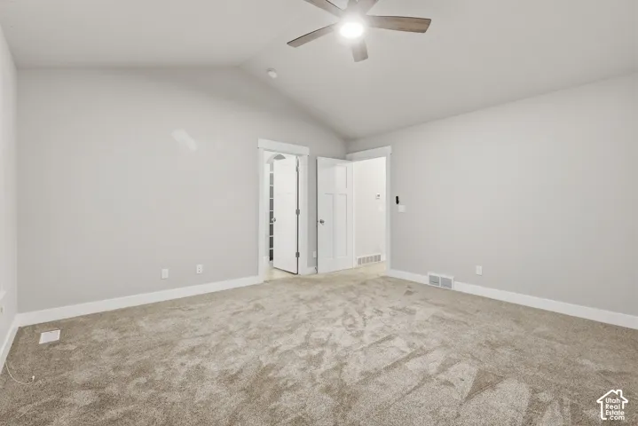 Vaulted ceiling with an attached ceiling fan, neutral wall finishes, and plush carpet flooring