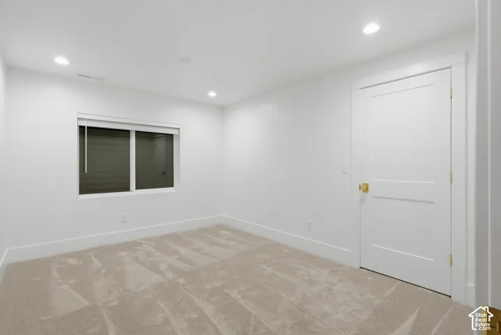 Recessed lighting, light-colored carpet, white trim, white paneled door with brass hardware, and a window with blinds