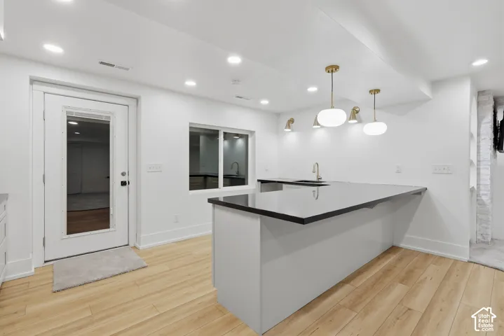 Spacious kitchen featuring a large island with black countertop, gold-finish pendant lighting, wood-finish flooring, and recessed lighting