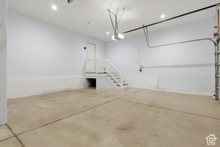 Spacious garage with an automatic door opener, concrete flooring, recessed lighting, and a white interior staircase with a railing