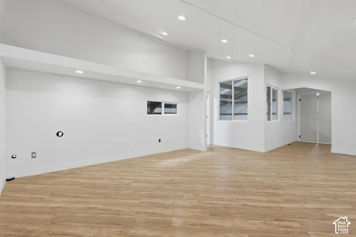 Vaulted ceilings with recessed lighting, wood-finish flooring, multiple windows, and crisp white walls