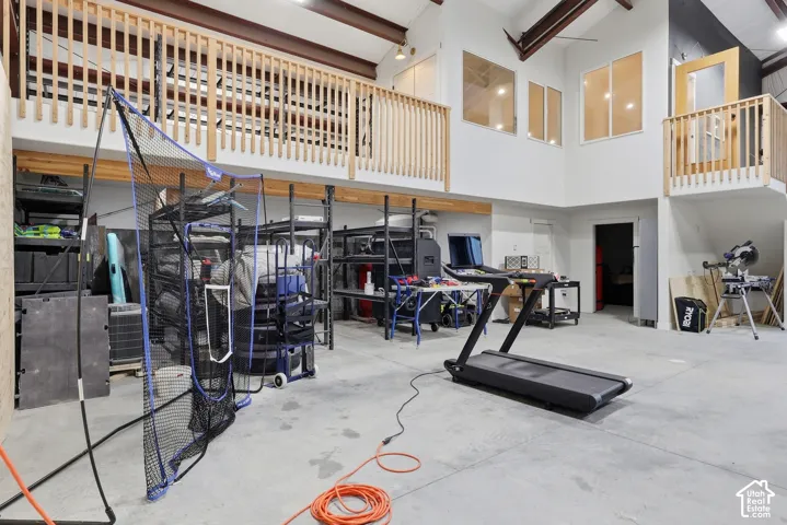 High ceilings with exposed structural beams, upper-level interior balconies with wood railings, multiple windows providing natural light, and a concrete floor
