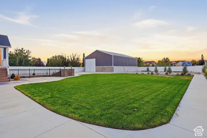 Expansive manicured lawn with concrete pathways, enclosed by a white privacy fence and black metal fencing