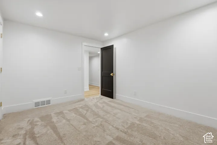 Recessed lighting illuminating a carpeted floor, white walls, and a dark paneled door