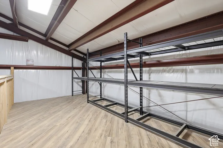 High-sloped ceiling with exposed structural beams, skylight, and wood-finish flooring