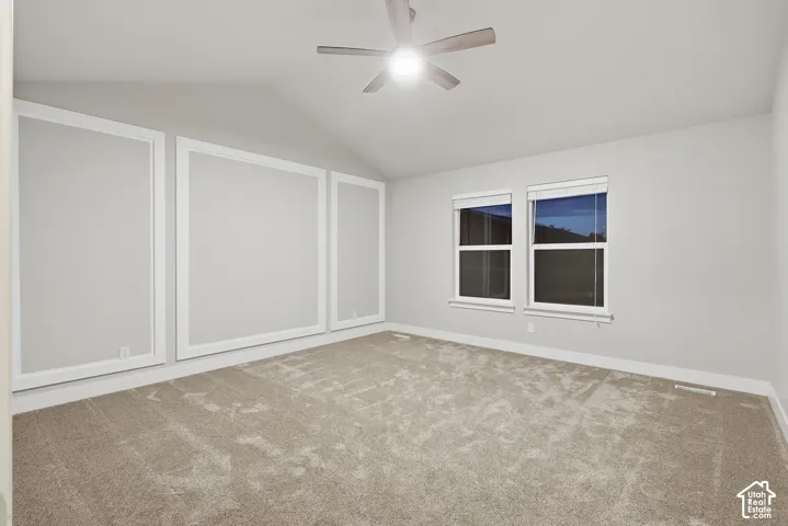Vaulted ceiling with a ceiling fan, carpeted flooring, two windows with blinds, and decorative wall trim