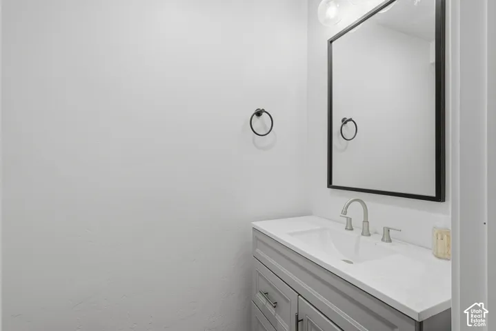 Vanity featuring a white countertop, undermount sink, brushed nickel faucet, gray cabinetry, and a framed mirror