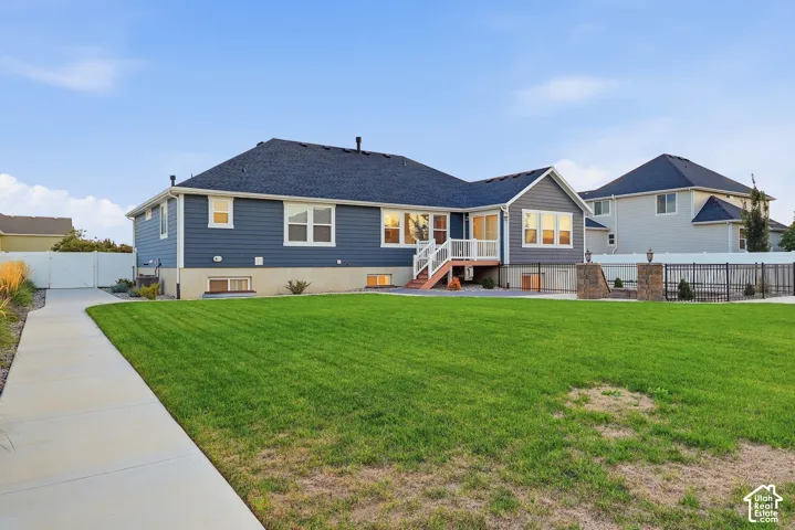 Expansive lawn with a concrete pathway, a two-story residence with blue siding, a dark roof, and a white deck with stairs