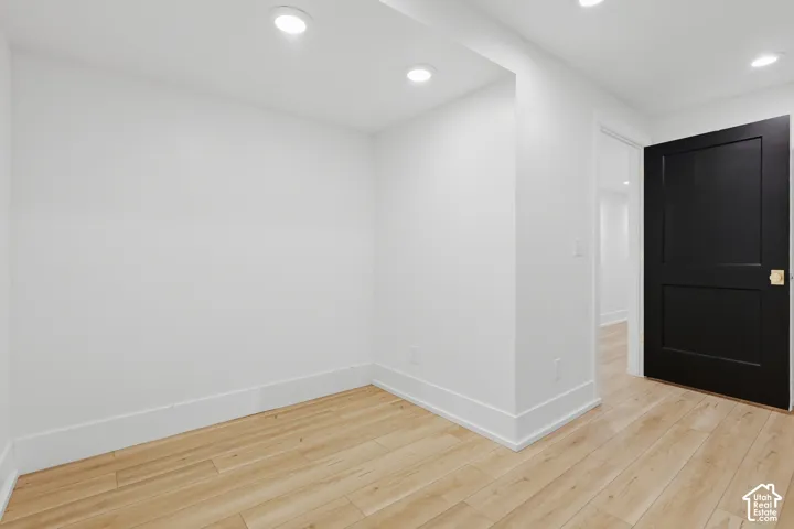 Recessed ceiling lighting, wood-finish flooring, white walls, white trim, and a black paneled door with brass hardware