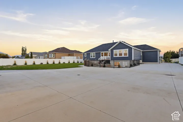 Expansive concrete paving with a contemporary blue siding exterior, a white vinyl fence, green lawn, and a multi-level deck featuring black railings