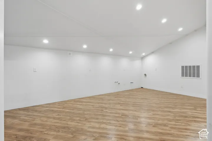 Wood-finish flooring, white walls, and a vaulted ceiling with recessed lighting