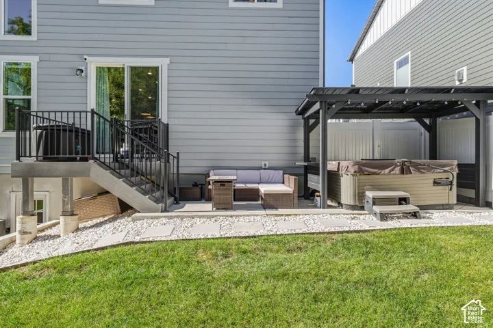 Paved patio area featuring a hot tub under a shaded pergola, a concrete staircase with black metal railings, and a sliding glass door for outdoor access