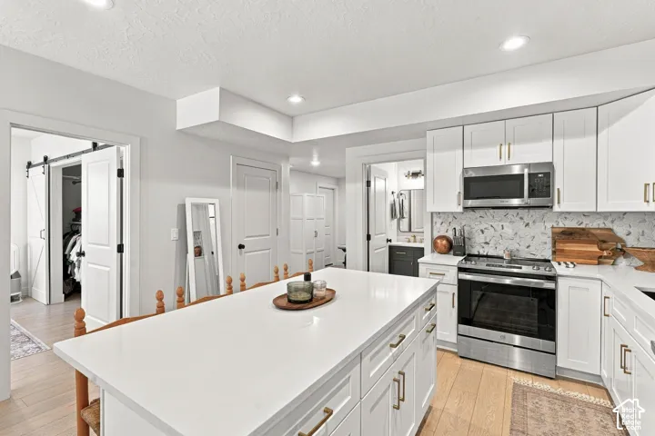 White cabinetry with gold-finish hardware, stainless steel appliances, and a quartz countertop island