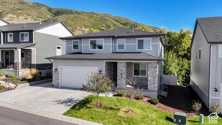 Two-story residence featuring a two-car garage, stone and siding exterior, front porch, and mature landscaping