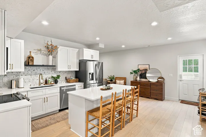 White shaker-style cabinetry, stainless steel appliances, light wood-finish flooring, recessed lighting, and a white kitchen island with counter seating