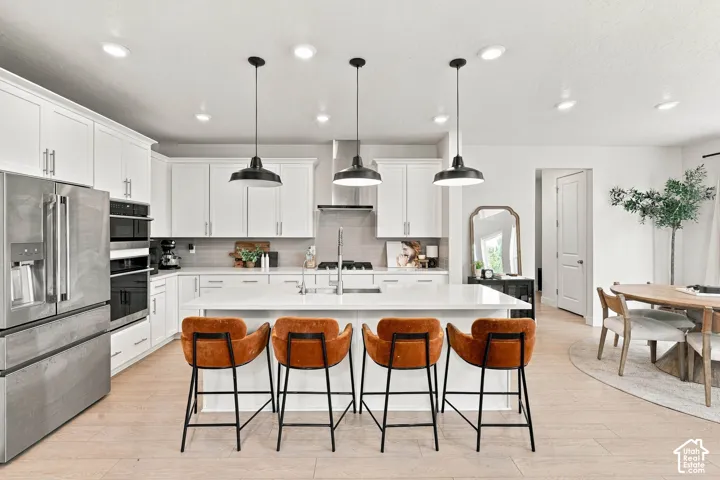 Stainless steel appliances, white cabinetry, recessed lighting, a kitchen island with seating, and wood-finish flooring
