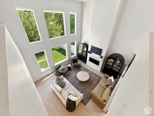 Two-story ceiling with multiple windows, light wood-finish flooring, and a built-in fireplace with a white mantel