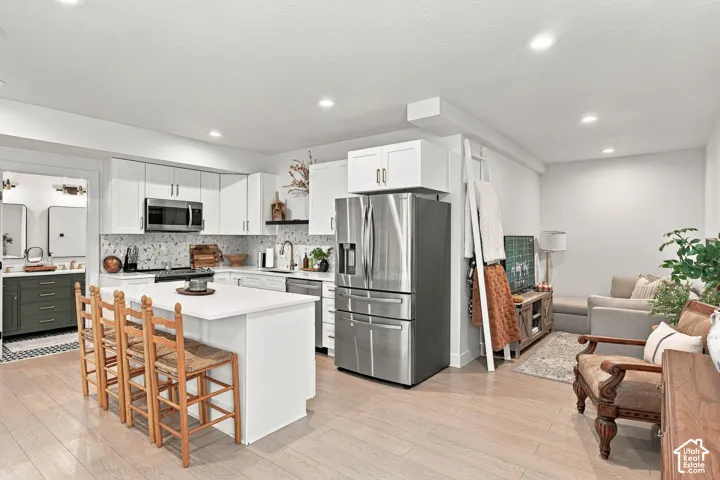 Open-concept living space with light wood-finish flooring, recessed lighting, and white cabinetry