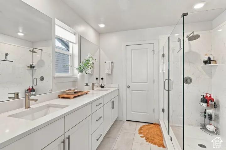 Dual vanity with undermount sinks and extensive countertop space, complemented by a glass-enclosed shower with a rainfall showerhead and wall-mounted shelving