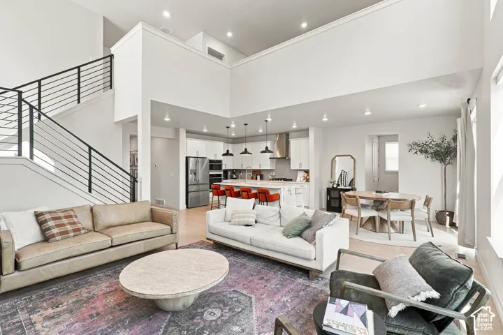 Open-concept living area with light-toned wood-finish flooring, high ceilings, and recessed lighting