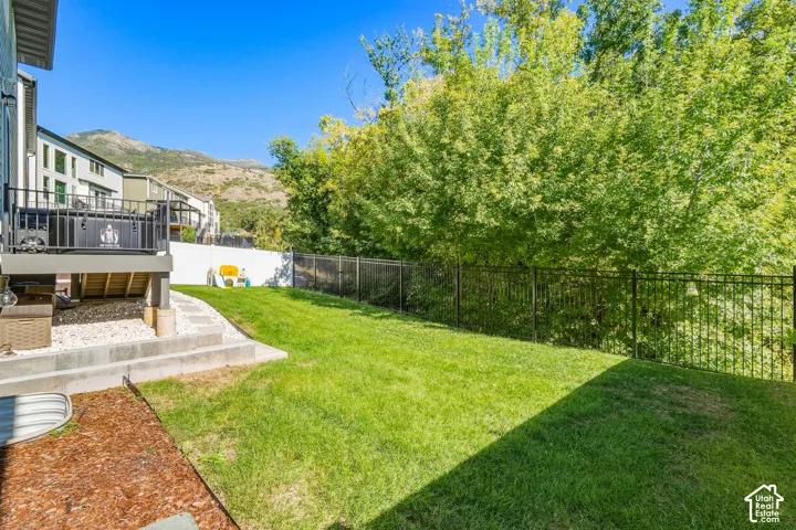Expansive backyard featuring a manicured lawn, multi-level composite deck, and a black wrought iron fence
