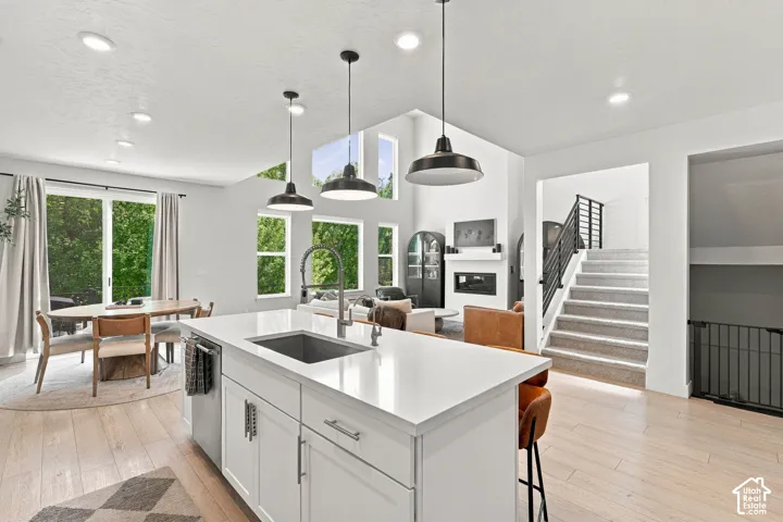 Kitchen island with integrated sink, white cabinetry, wood-finish flooring, recessed lighting, and black pendant lights