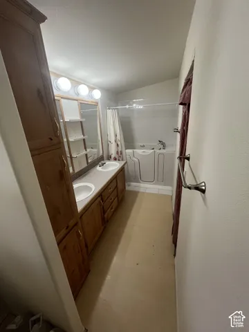 Dual vanity with integrated sinks, wood-finish cabinetry, built-in storage cabinet, and walk-in bathtub