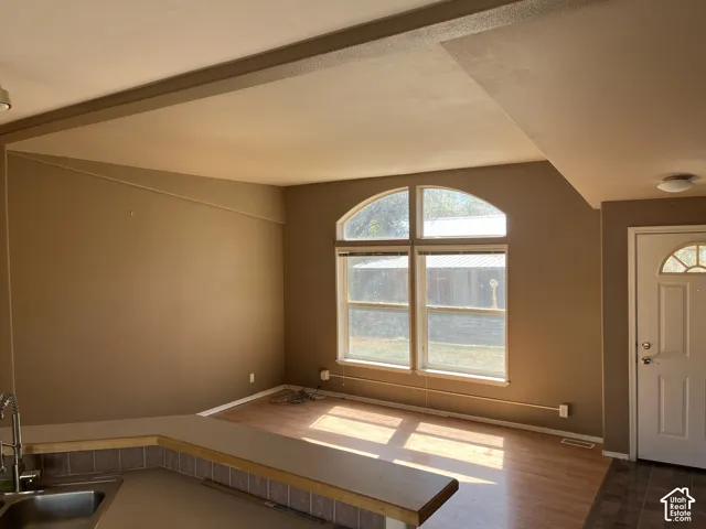 Open-concept living area with wood-finish flooring, an arched picture window, and a breakfast bar with tile backsplash
