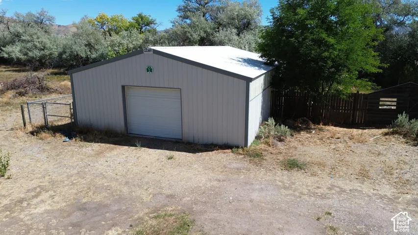 Metal outbuilding with a roll-up garage door, a sloped roof, and a partial perimeter fence