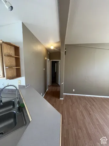 Wood-finish flooring throughout, track lighting, dual basin stainless steel sink with a high-arc faucet, and an open wall cabinet
