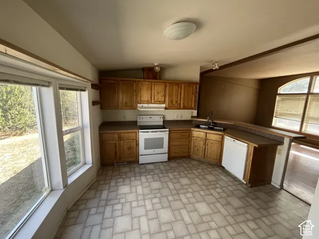 Kitchen featuring wood cabinetry, a white appliance suite, dual basin sink, and a breakfast bar