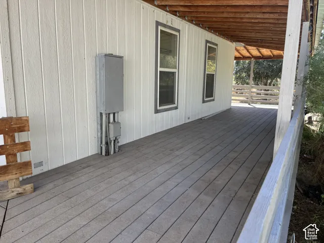 Expansive covered porch featuring a planked deck, white vertical siding, and exposed wood ceiling beams