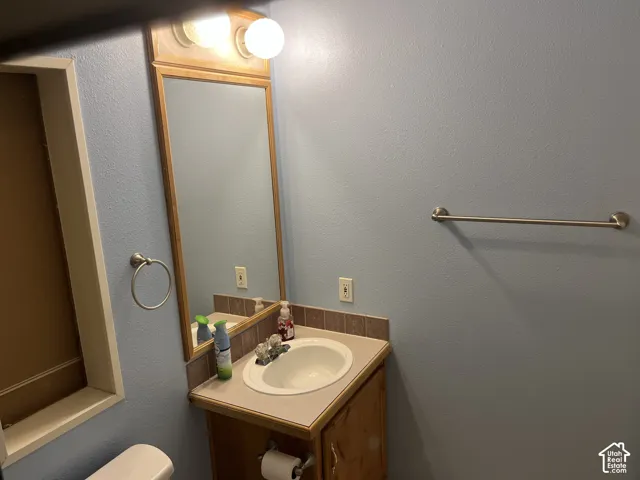 Vanity with integrated sink, wood-finish cabinetry, and tiled backsplash