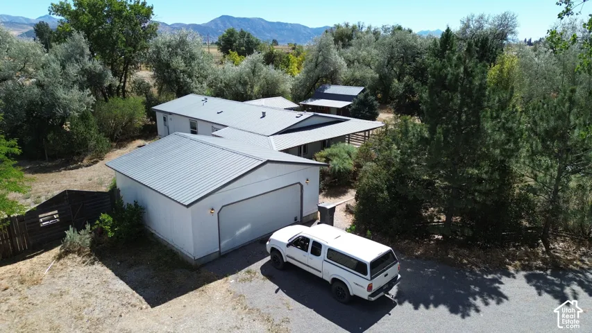 White exterior with a metal roof, attached garage, and mature landscaping
