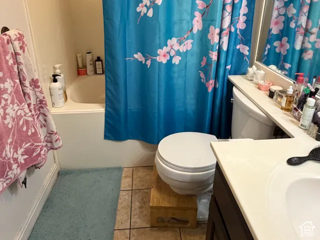 Built-in bathtub with shower, toilet, tile flooring, and a single-sink vanity with a dark wood-finish cabinet