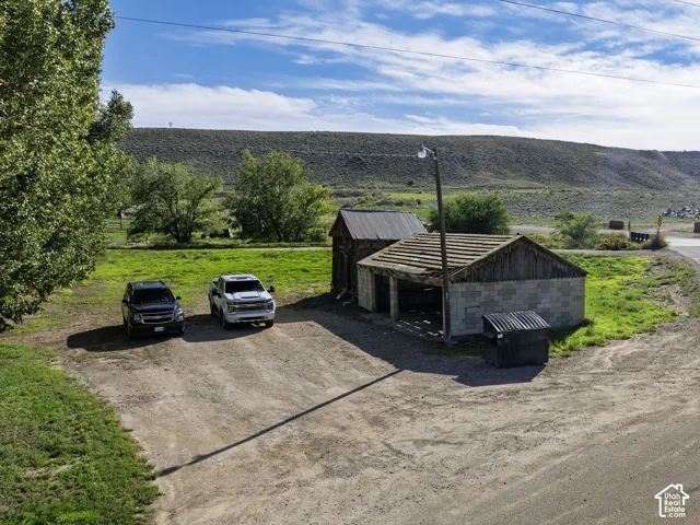 Gravel driveway with two vehicles, a concrete block outbuilding with an open-sided structure, and a wooden outbuilding