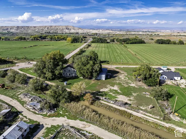 Expansive green fields, a visible dirt road, a substantial body of water, and distant natural landforms