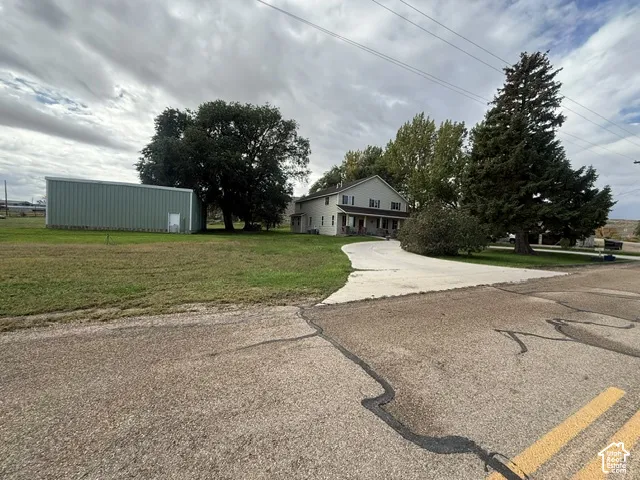 Two-story residence with a covered front porch, a curved concrete driveway, mature trees, and a substantial metal-sided outbuilding