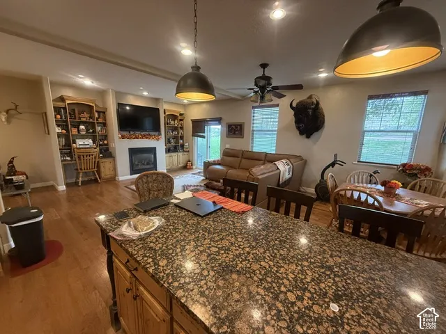 Granite kitchen island with recessed lighting, wood-finish flooring, built-in shelving, and a fireplace with a mantel