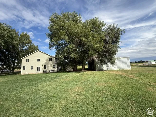 Expansive green lawn featuring a two-story residence with light-colored siding, a detached metal utility building, and mature trees