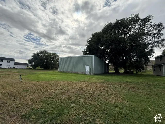 Expansive green space featuring a large metal-sided outbuilding with a white entrance door and a mature tree