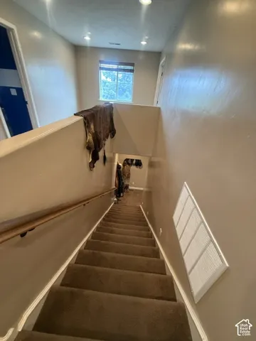 Carpeted staircase with a wood handrail, recessed lighting, and a window providing natural illumination