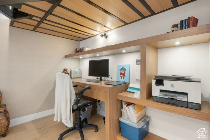 Integrated wood-finish desk and shelving unit with recessed lighting, complemented by a slatted wood-finish ceiling with dark metal accents, and wood-finish flooring