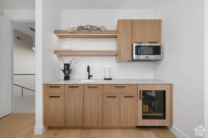 Built-in bar area featuring light wood-finish cabinetry, a stone countertop, a sink with a matte black faucet, and a beverage refrigerator