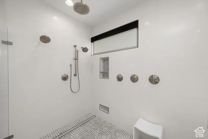 Spacious shower with multiple shower heads, sleek white tiling, integrated shower niche, and mosaic tile flooring