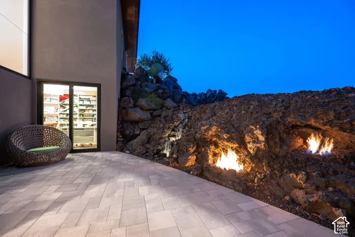 Pavered patio area with a natural rock wall featuring built-in fire elements and a water feature
