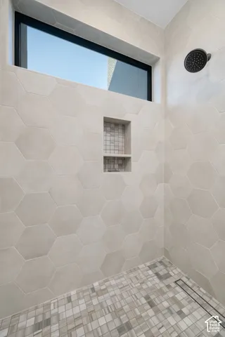 Hexagonal wall tile with a recessed niche, linear floor drain, and a black showerhead