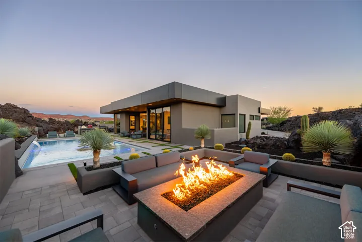 Modern exterior architecture with expansive glass panels, a paver patio, a built-in fire pit, a rectangular swimming pool, and desert landscaping